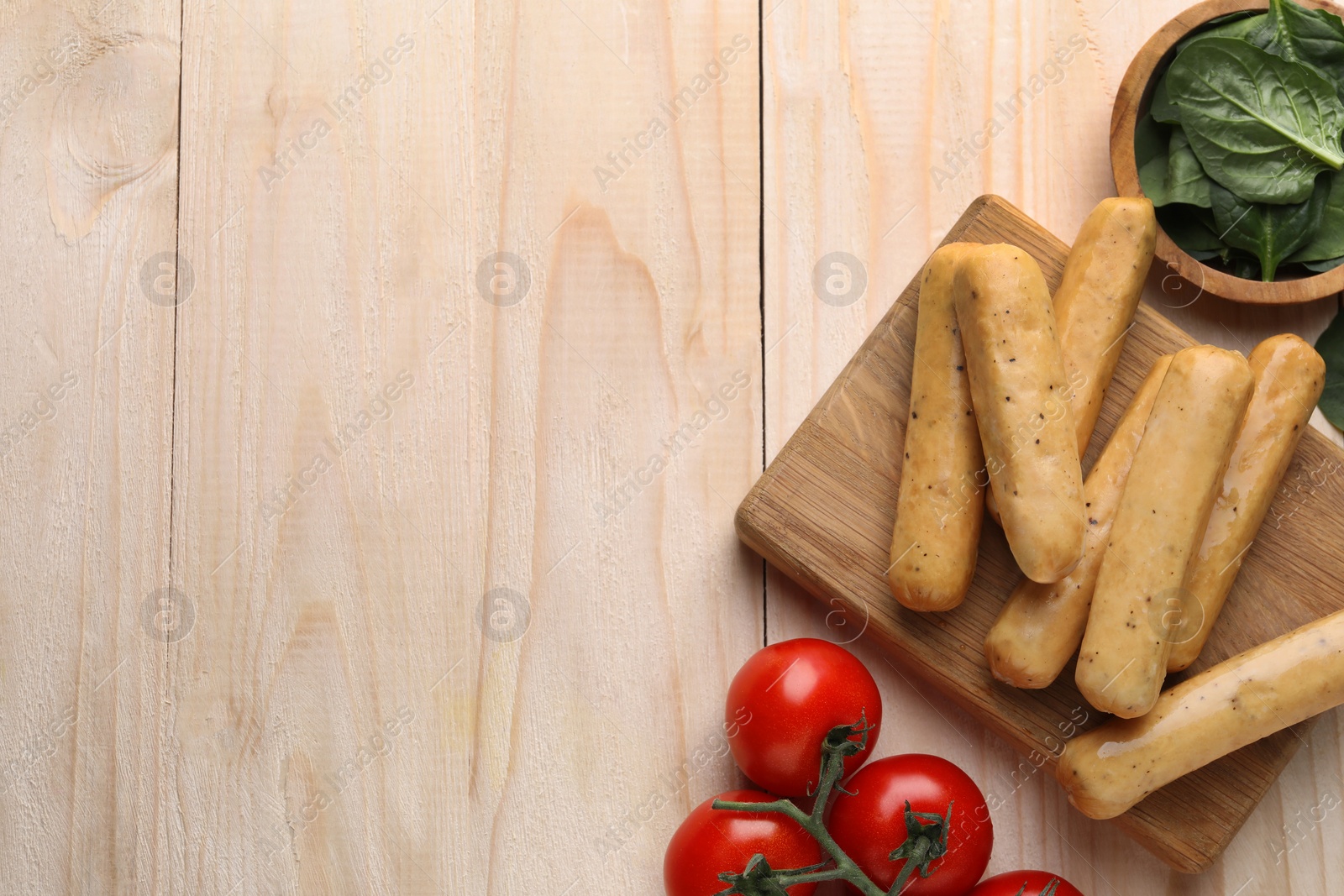 Photo of Raw vegan sausages with tomatoes and spinach on wooden table, flat lay. Space for text