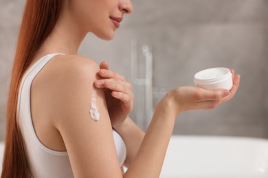 Young woman applying body cream onto shoulder in bathroom, closeup