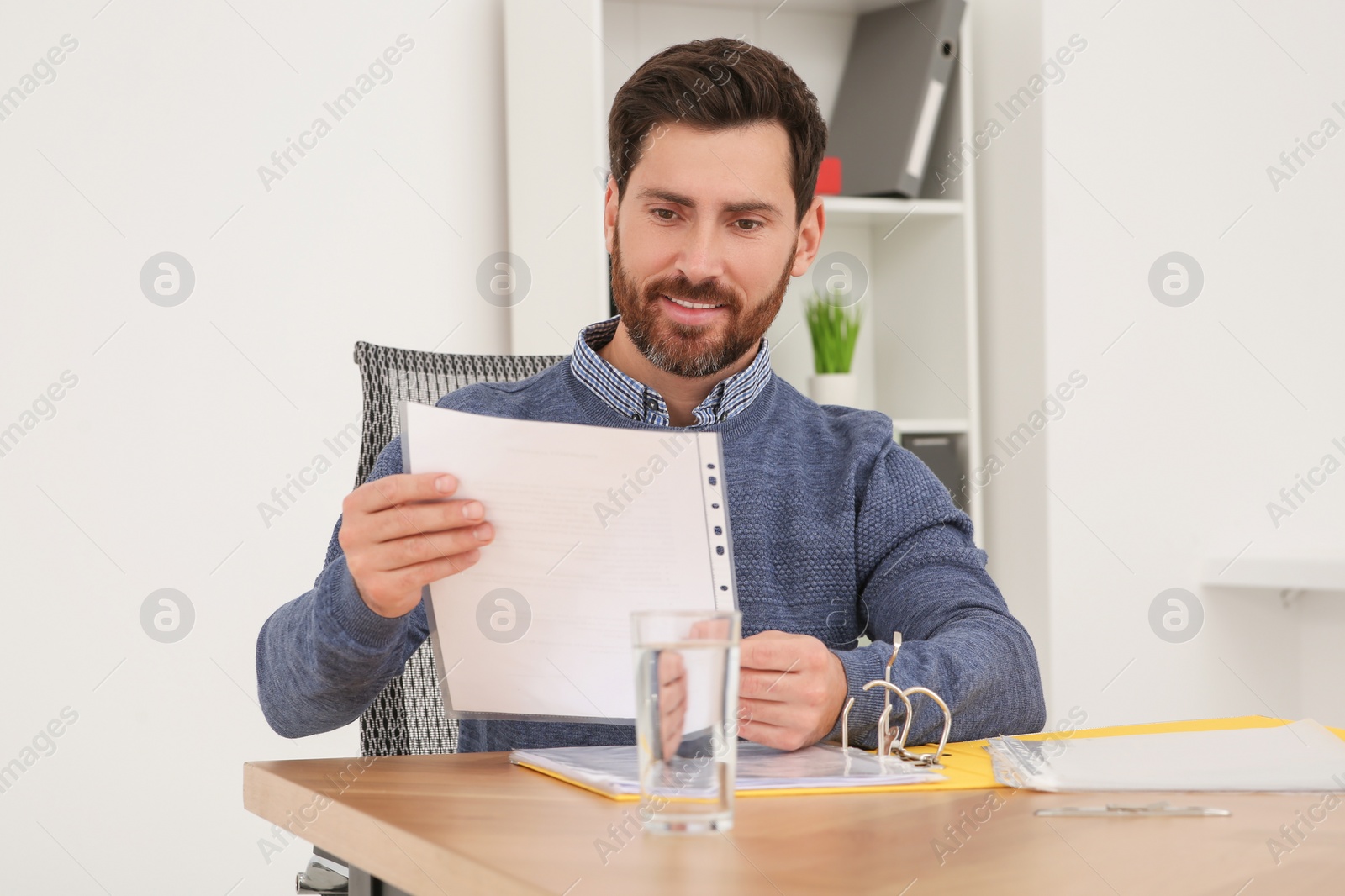 Photo of Businessman reading document at wooden table in office