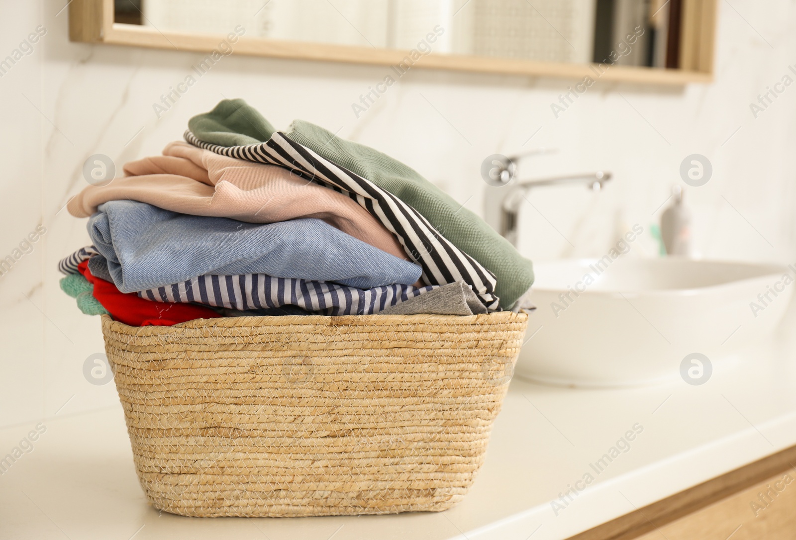 Photo of Wicker basket with laundry on countertop in bathroom