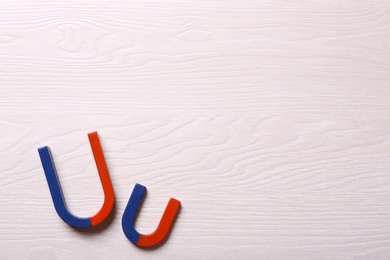 Photo of Red and blue horseshoe magnets on light wooden background, flat lay. Space for text