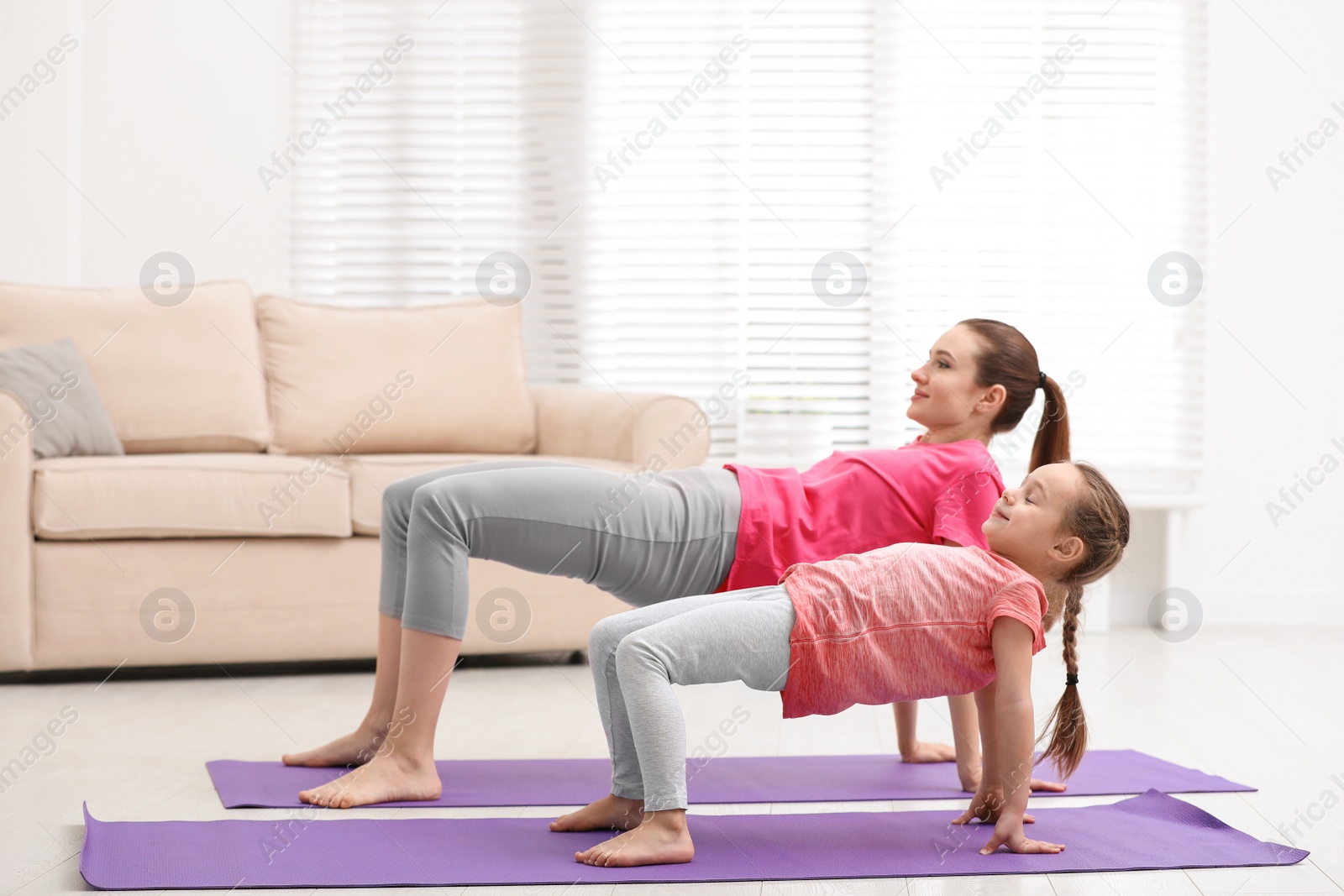 Photo of Young mother with little daughter practicing yoga at home