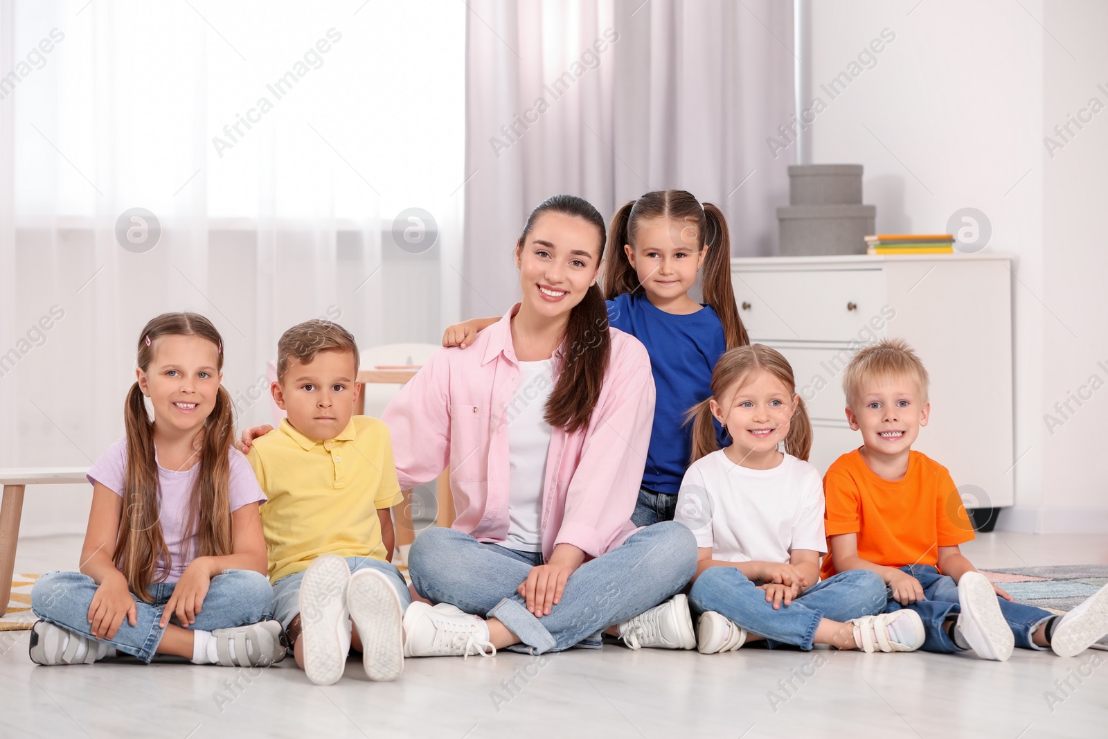 Photo of Happy nursery teacher and group of cute little children on floor in kindergarten. Playtime activities