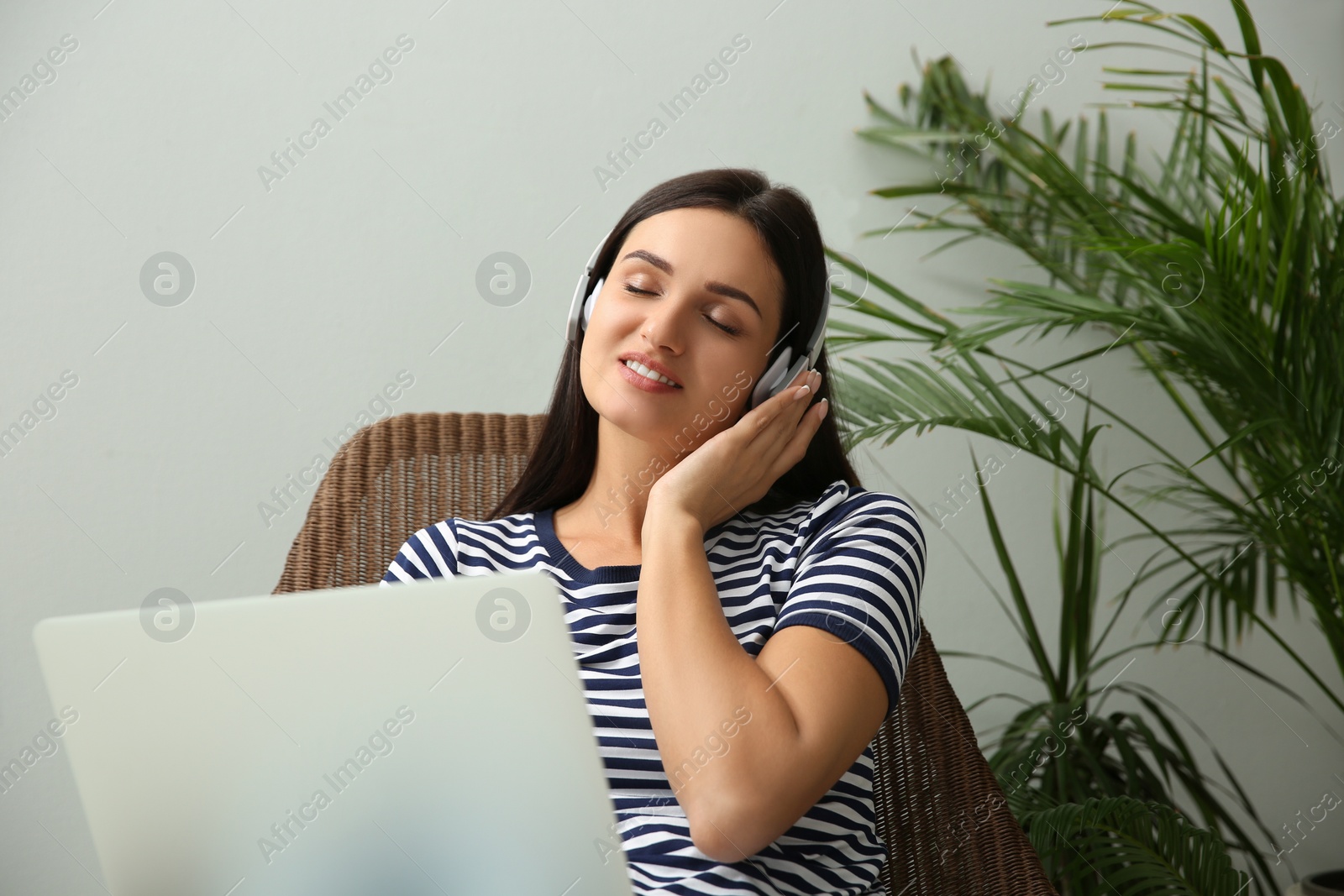 Photo of Young woman listening to music while working on laptop at home