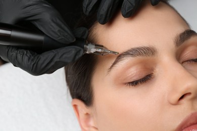 Beautician making permanent eyebrow makeup to young woman, closeup