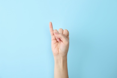 Woman showing I letter on color background, closeup. Sign language