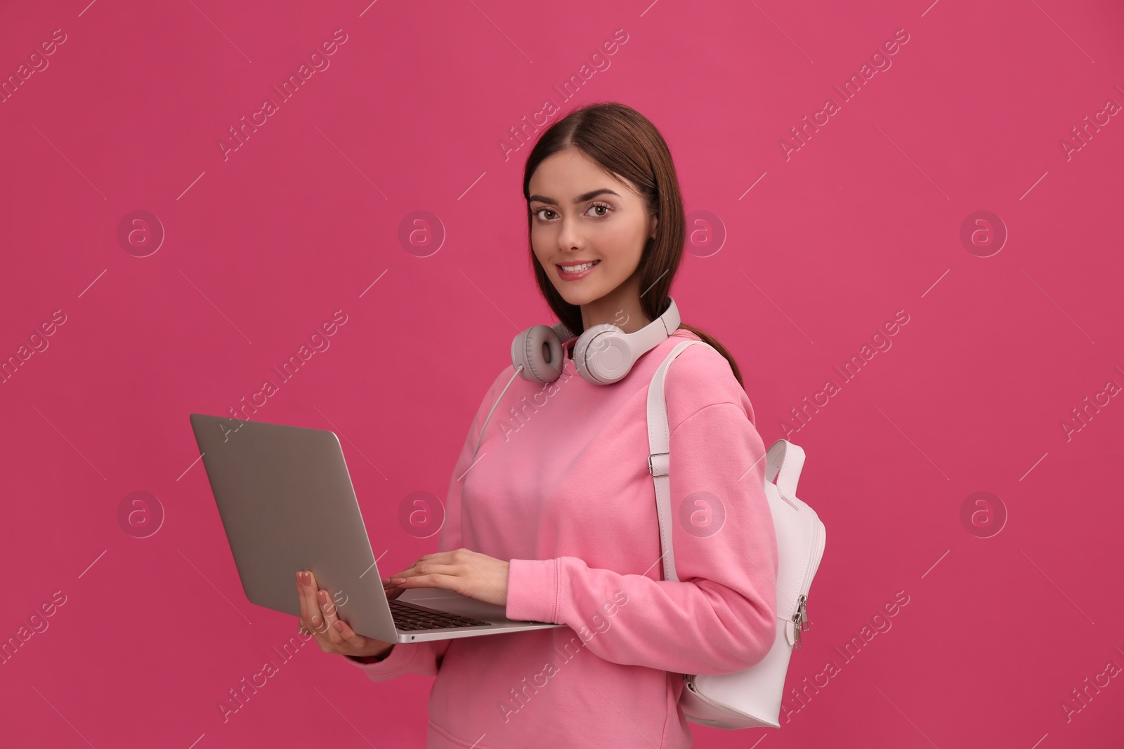 Photo of Teenage student with laptop, headphones and backpack on pink background