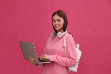 Teenage student with laptop, headphones and backpack on pink background