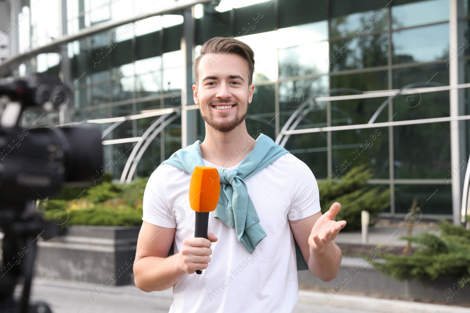 Photo of Young male journalist with microphone working on city street