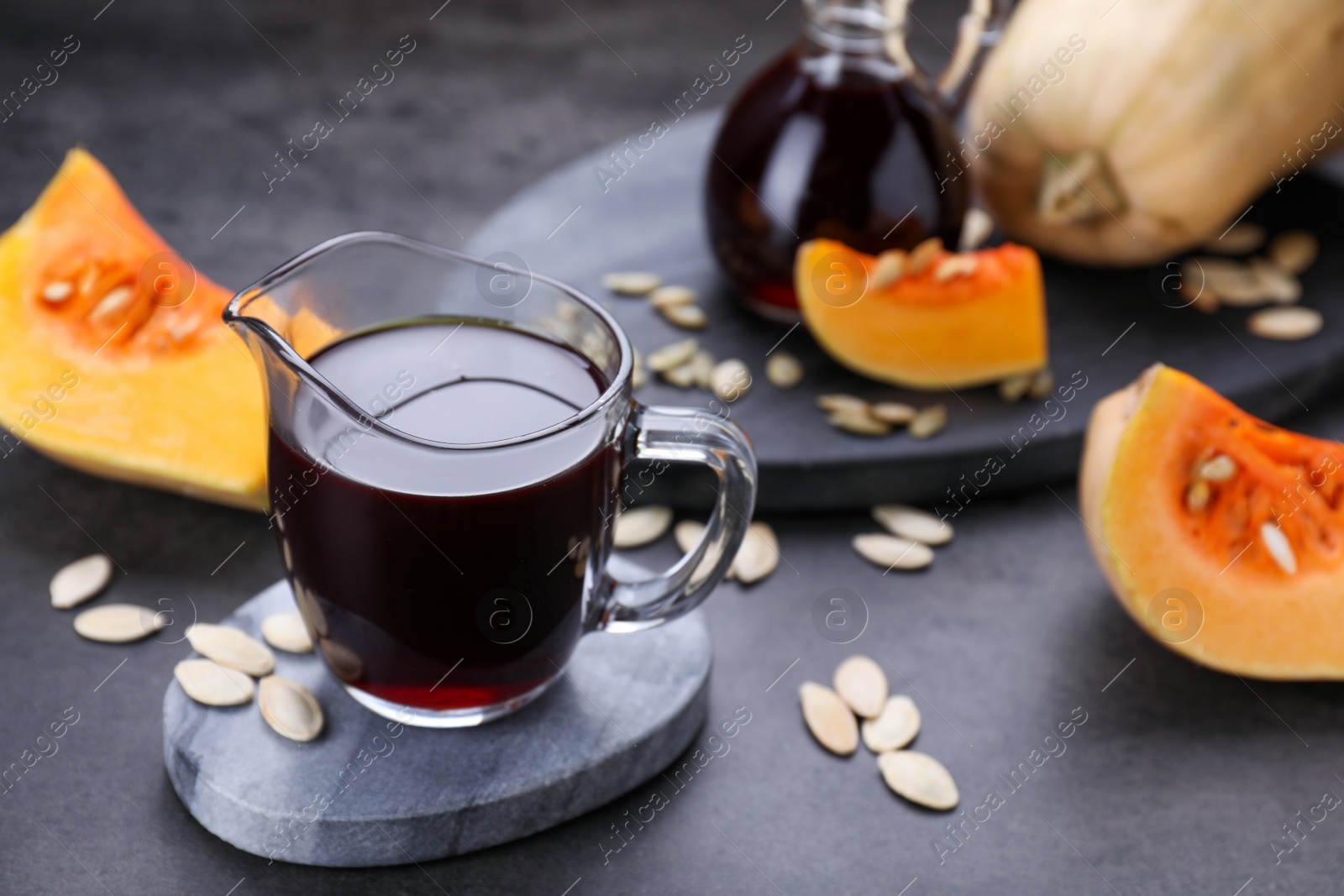 Photo of Fresh pumpkin seed oil in glass pitcher on dark grey table