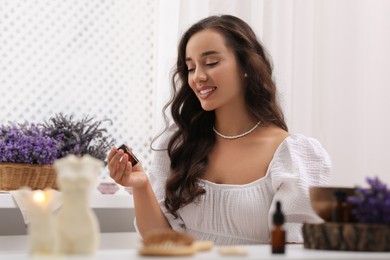 Photo of Beautiful young woman with bottle of essential oil at table indoors