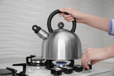 Woman putting kettle on gas stove in kitchen, closeup