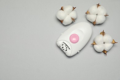 Modern epilator and fluffy cotton flowers on light grey background, flat lay. Space for text