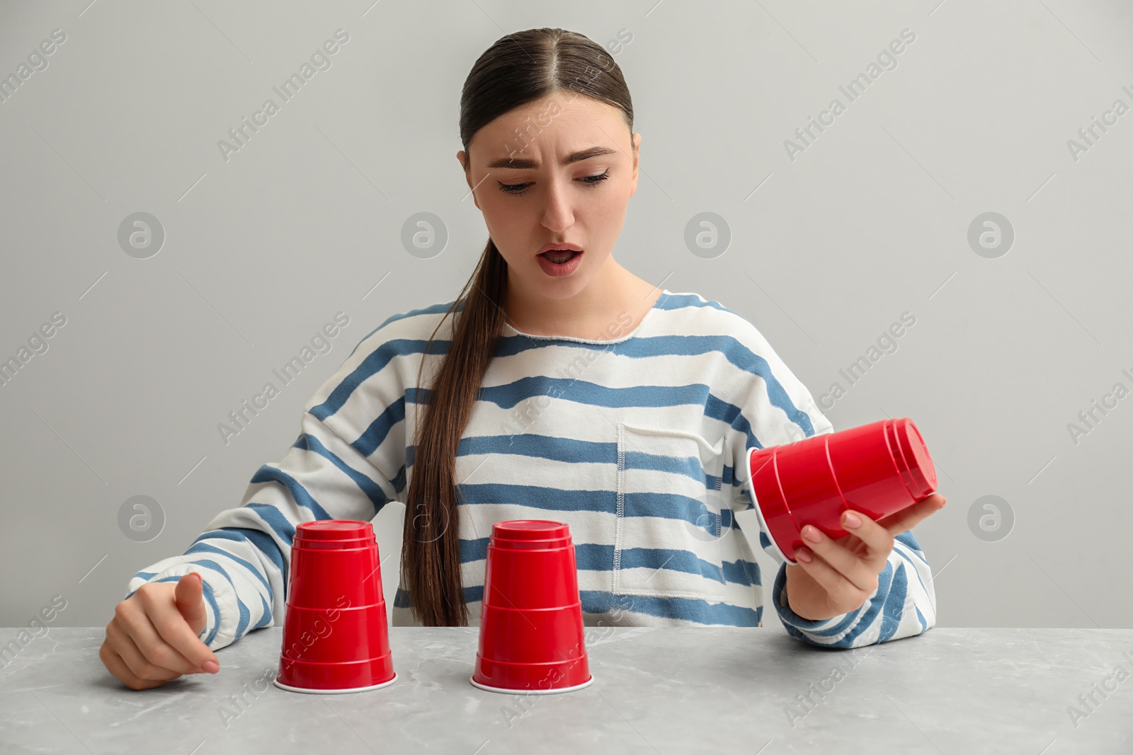Photo of Disappointed woman playing shell game at light marble table