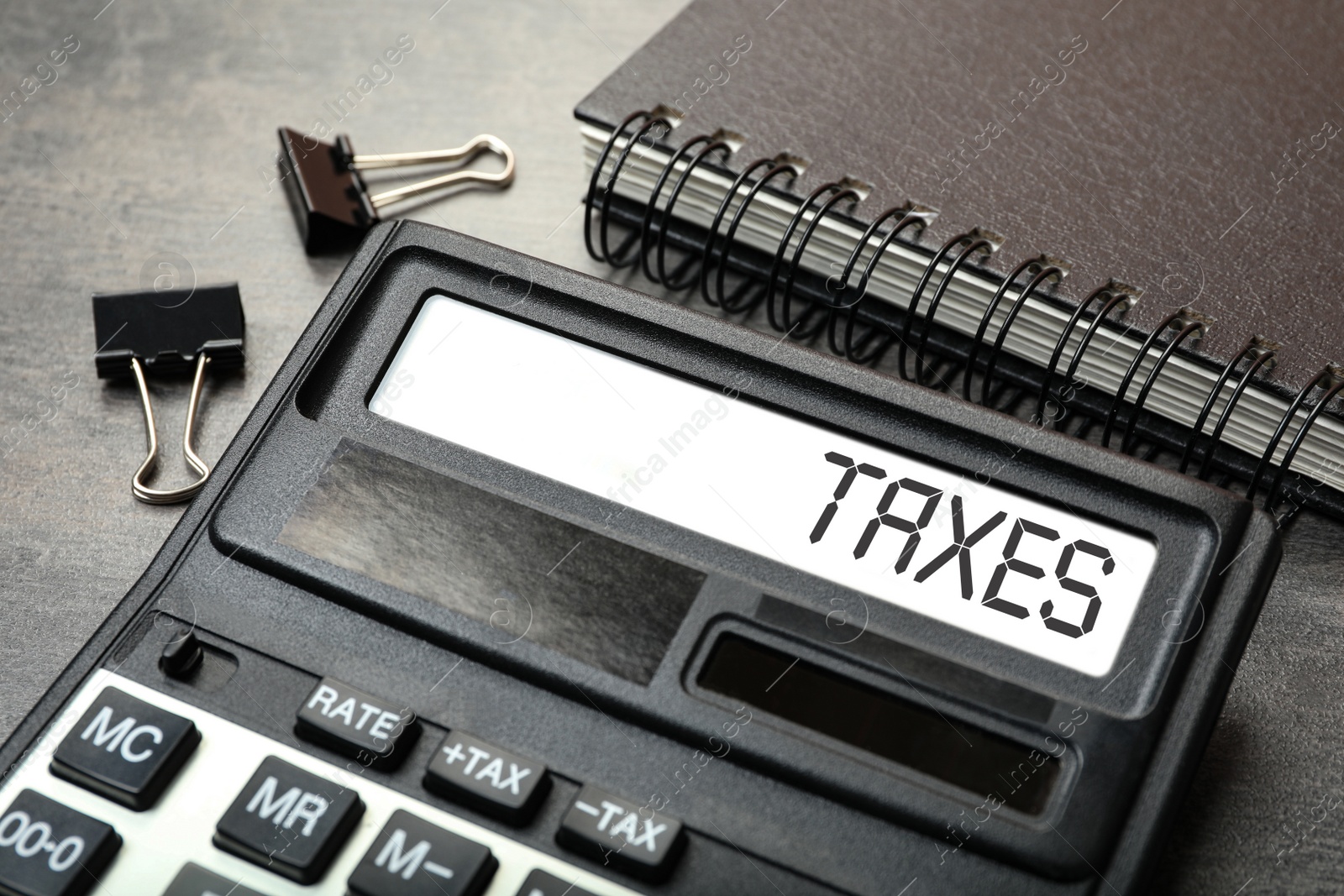 Image of Calculator with word Taxes, notebook and paper clips on table, closeup