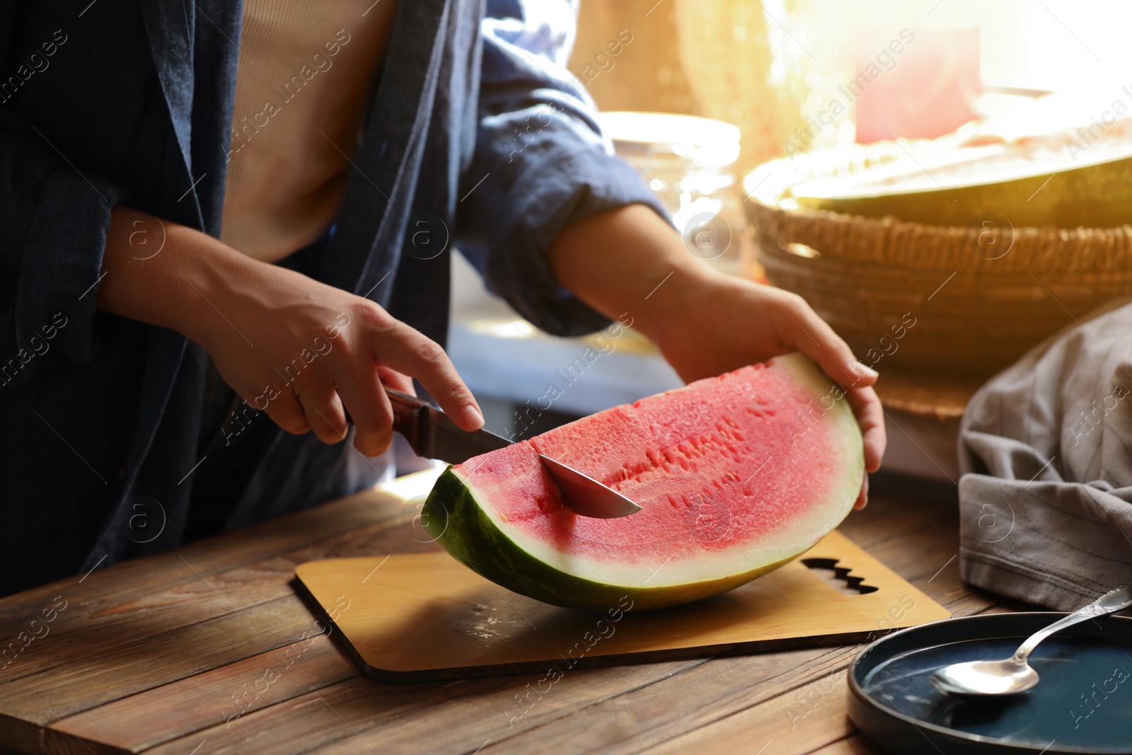 Photo of Woman cutting fresh juicy watermelon at wooden table, closeup