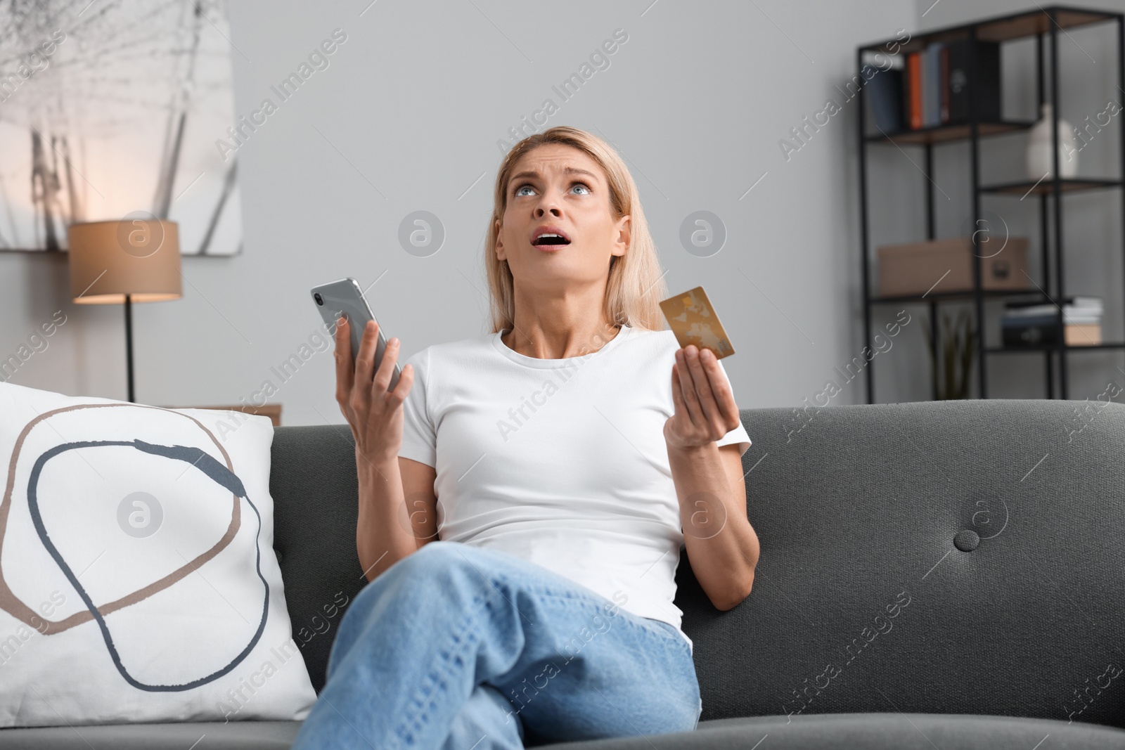 Photo of Emotional woman with credit card and smartphone on sofa at home. Be careful - fraud