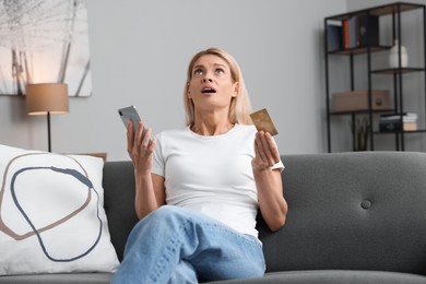 Photo of Emotional woman with credit card and smartphone on sofa at home. Be careful - fraud