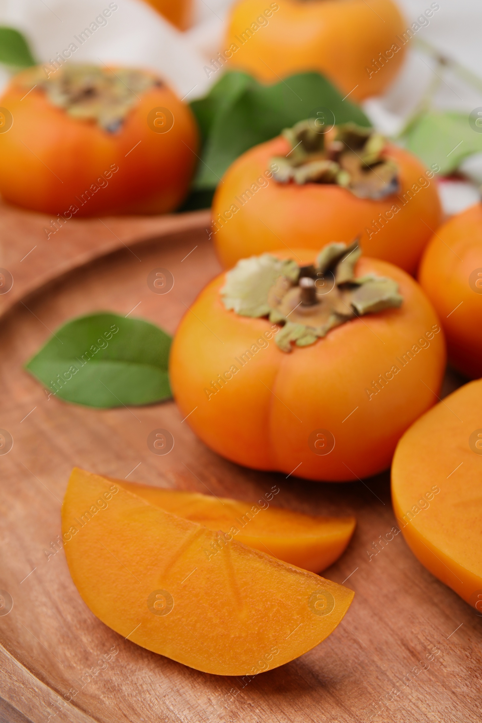 Photo of Wooden tray with whole and cut delicious ripe persimmons, closeup
