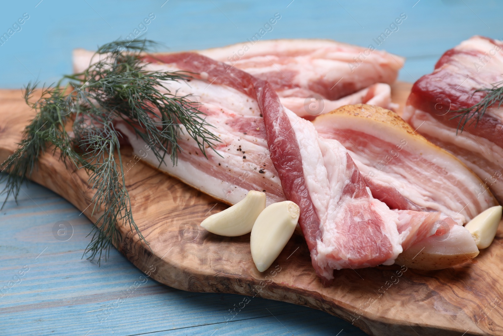 Photo of Pieces of pork fatback with garlic and dill on light blue wooden table, closeup