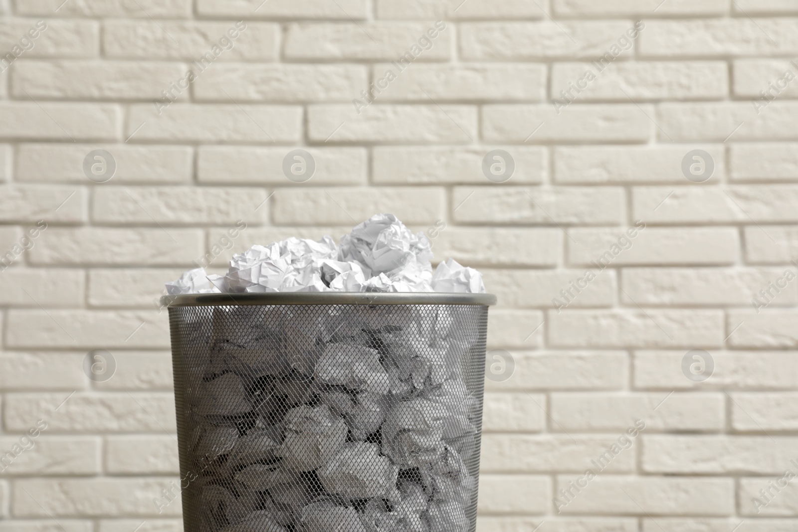 Photo of Metal bin with crumpled paper against brick wall, space for text