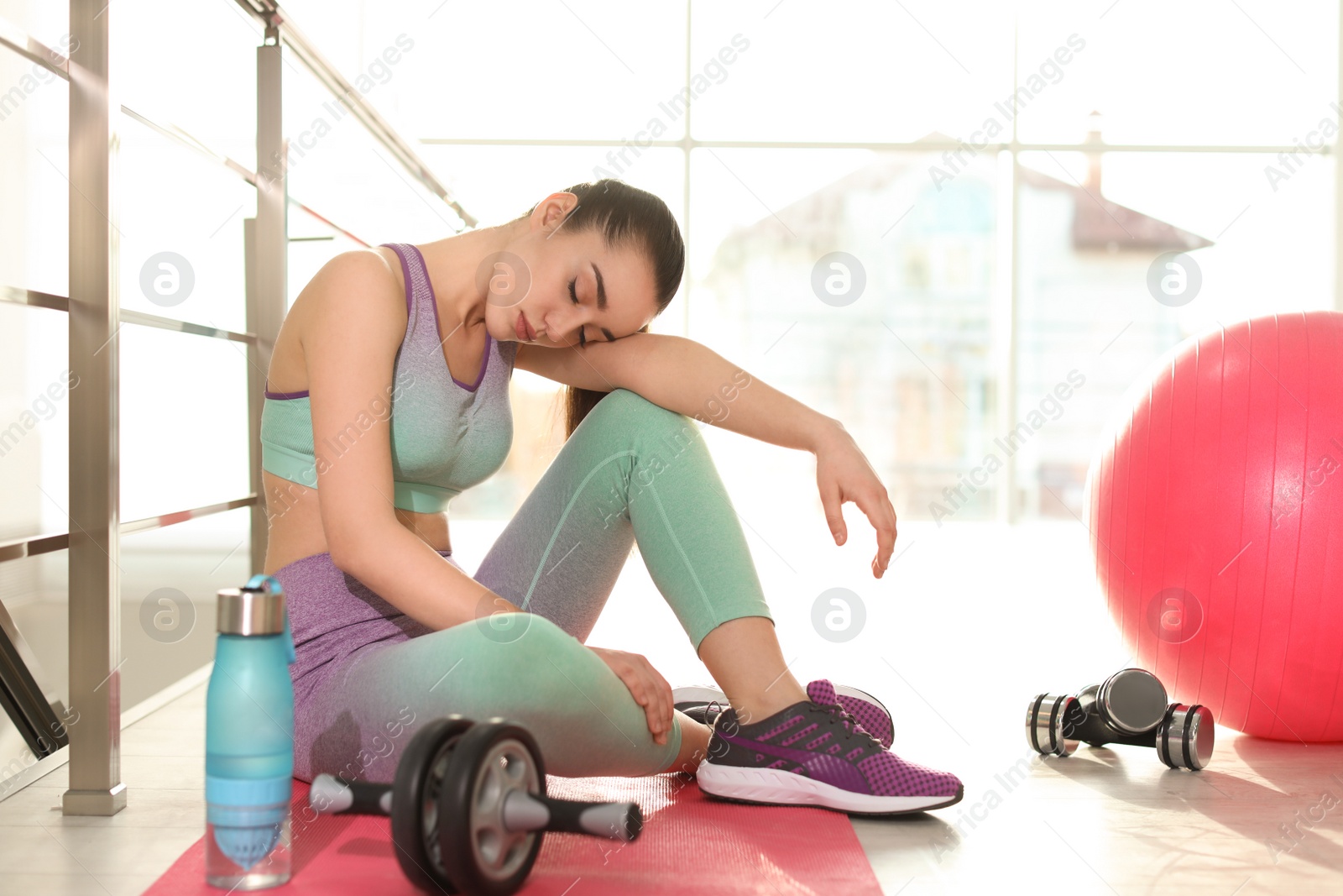 Photo of Lazy young woman with sport equipment on yoga mat indoors