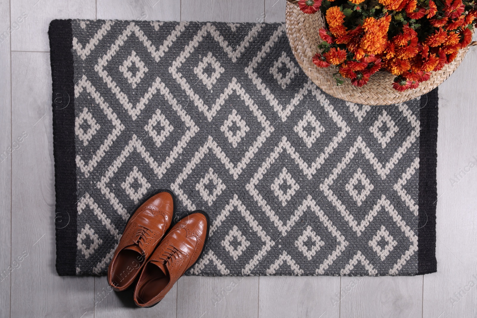 Photo of Stylish door mat with shoes and beautiful flowers on floor, flat lay