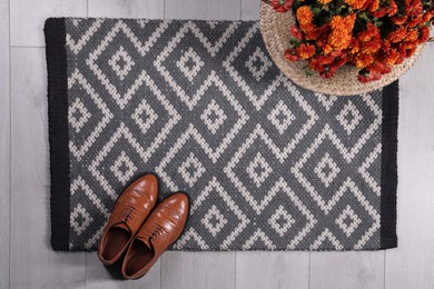 Stylish door mat with shoes and beautiful flowers on floor, flat lay