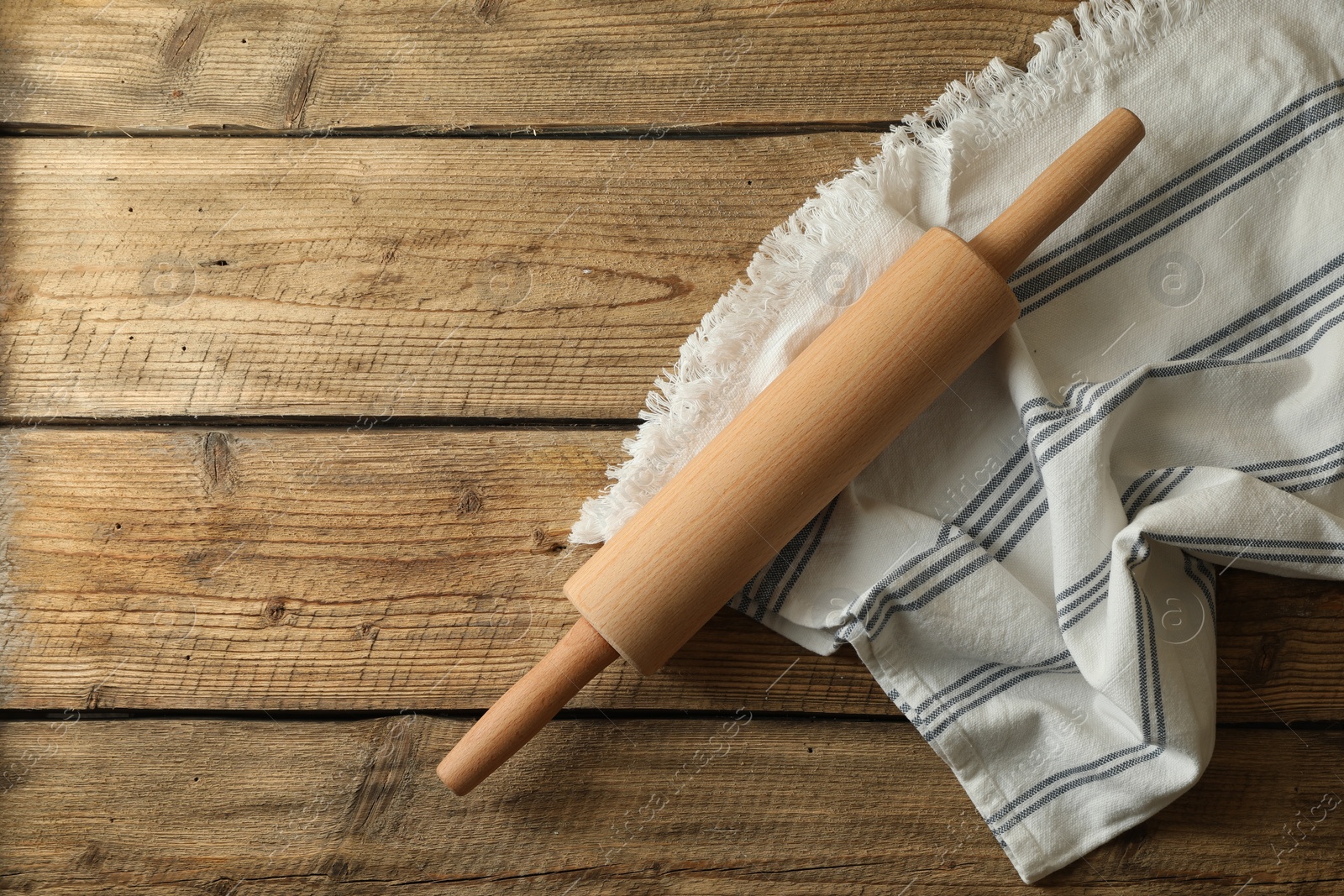 Photo of Rolling pin and kitchen towel on wooden table, top view. Space for text