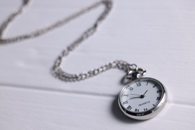 Silver pocket clock with chain on white wooden table, closeup