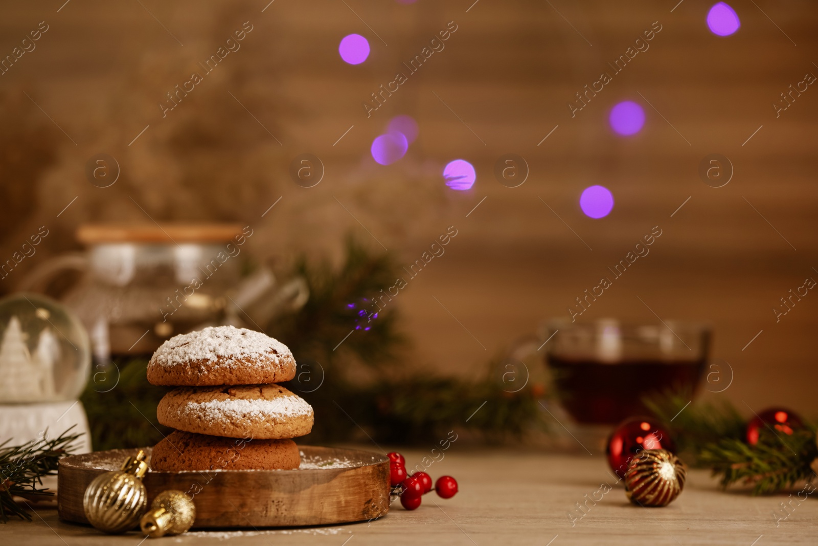 Photo of Delicious cookies and Christmas decor on wooden table against blurred festive lights, space for text