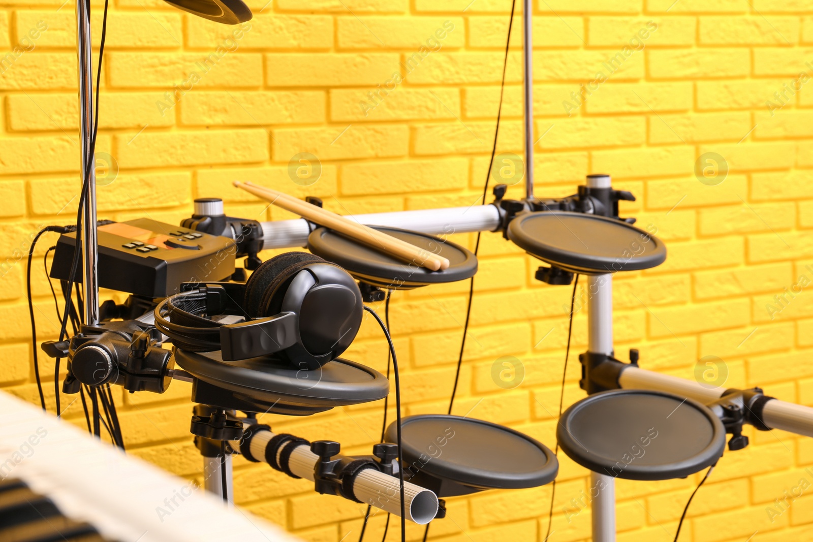 Photo of Modern electronic drum kit near yellow brick wall indoors. Musical instrument