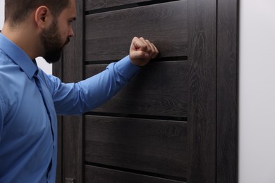 Collection agent in blue shirt knocking on wooden door