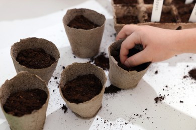 Photo of Little girl planting vegetable seeds into peat pots with soil at white table, closeup