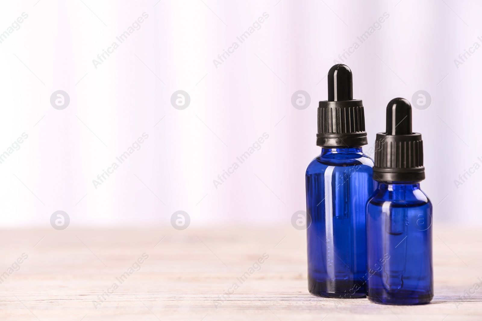 Photo of Bottles of essential oils on table against light background, space for text. Cosmetic products