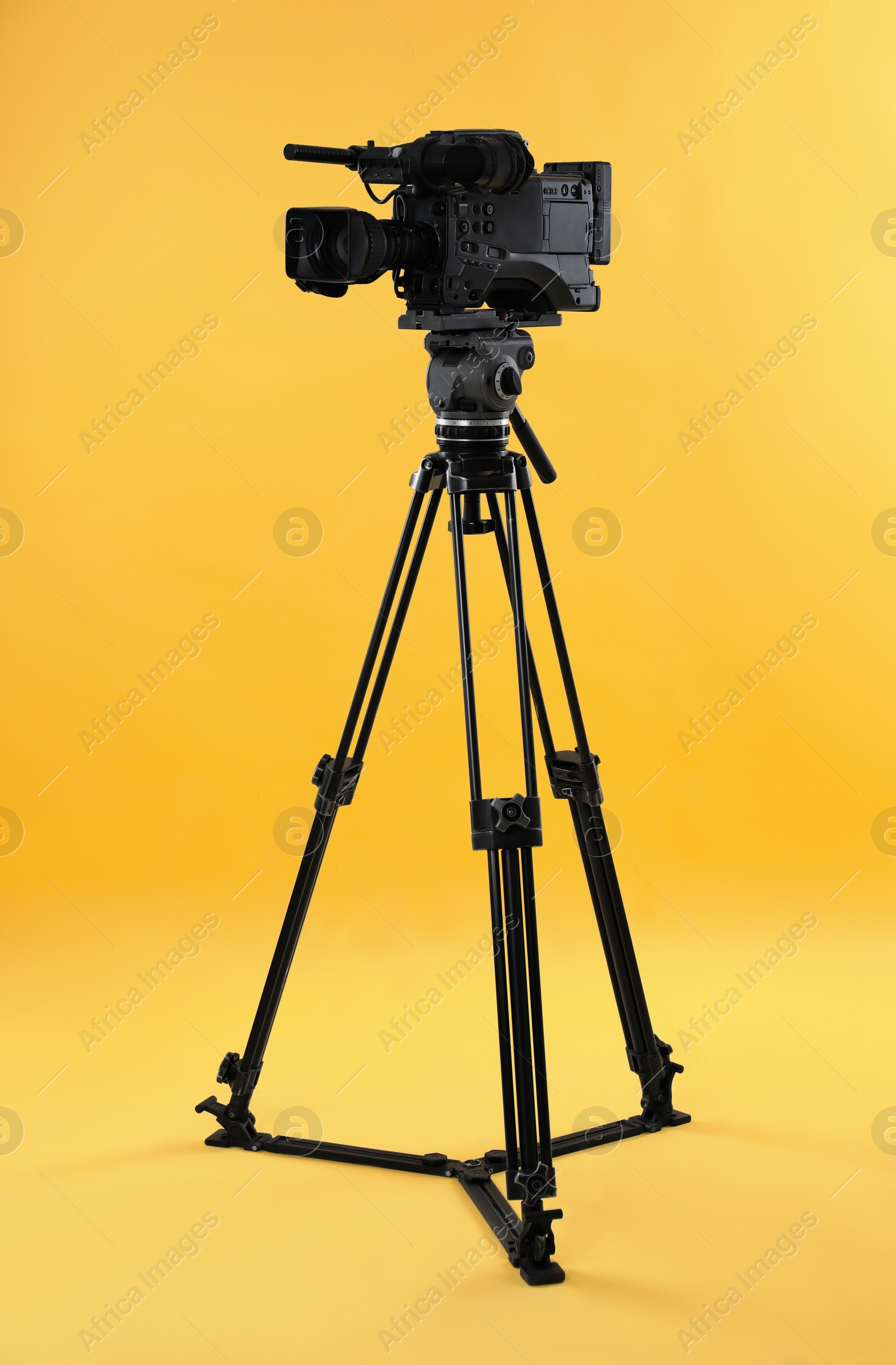Photo of Modern professional video camera on yellow background