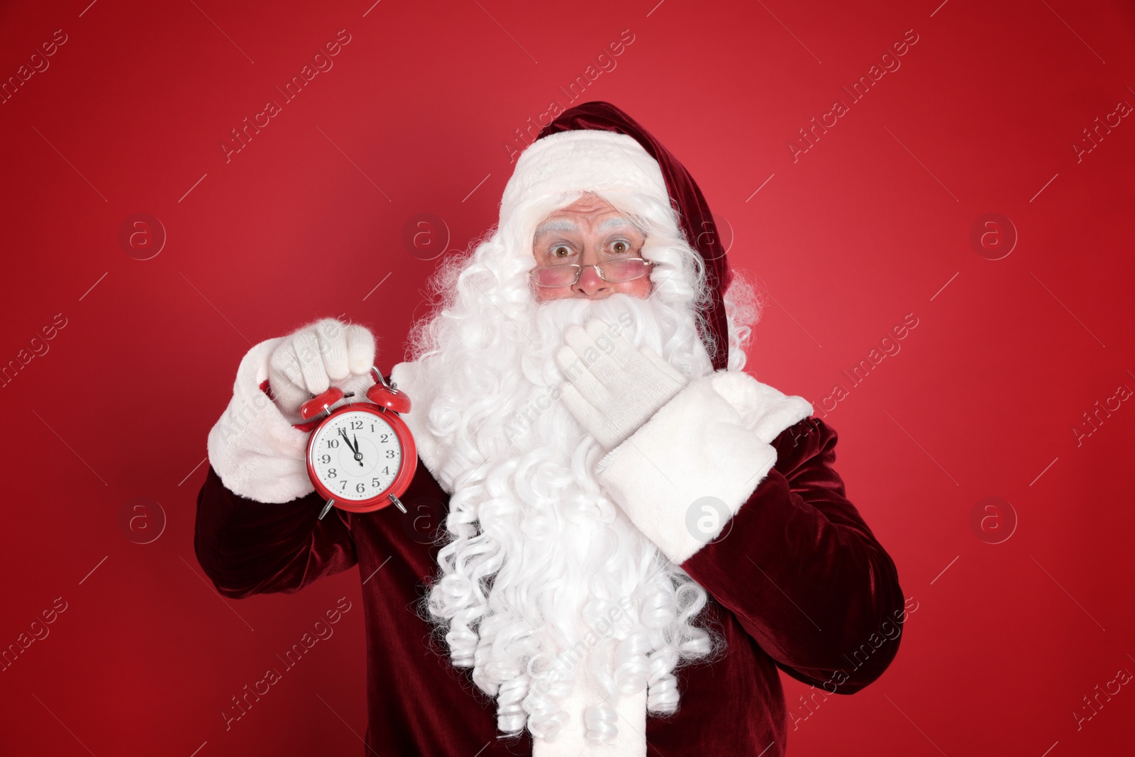 Photo of Santa Claus holding alarm clock on red background. Christmas countdown