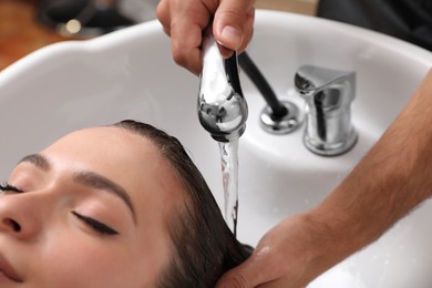 Photo of Professional hairdresser washing client's hair at sink indoors, closeup