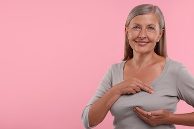 Beautiful senior woman doing breast self-examination on pink background, space for text