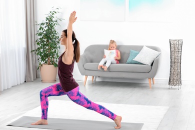 Woman doing fitness exercises while her daughter sitting on sofa at home