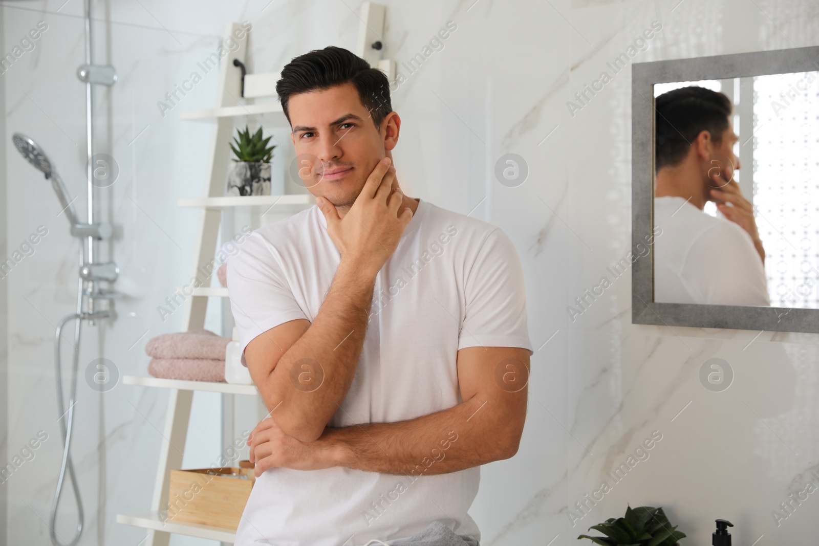 Photo of Handsome man touching his smooth face in bathroom after shaving