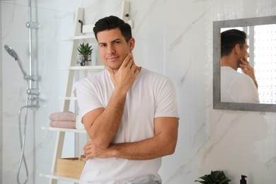 Handsome man touching his smooth face in bathroom after shaving