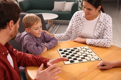 Family playing checkers at wooden table in room