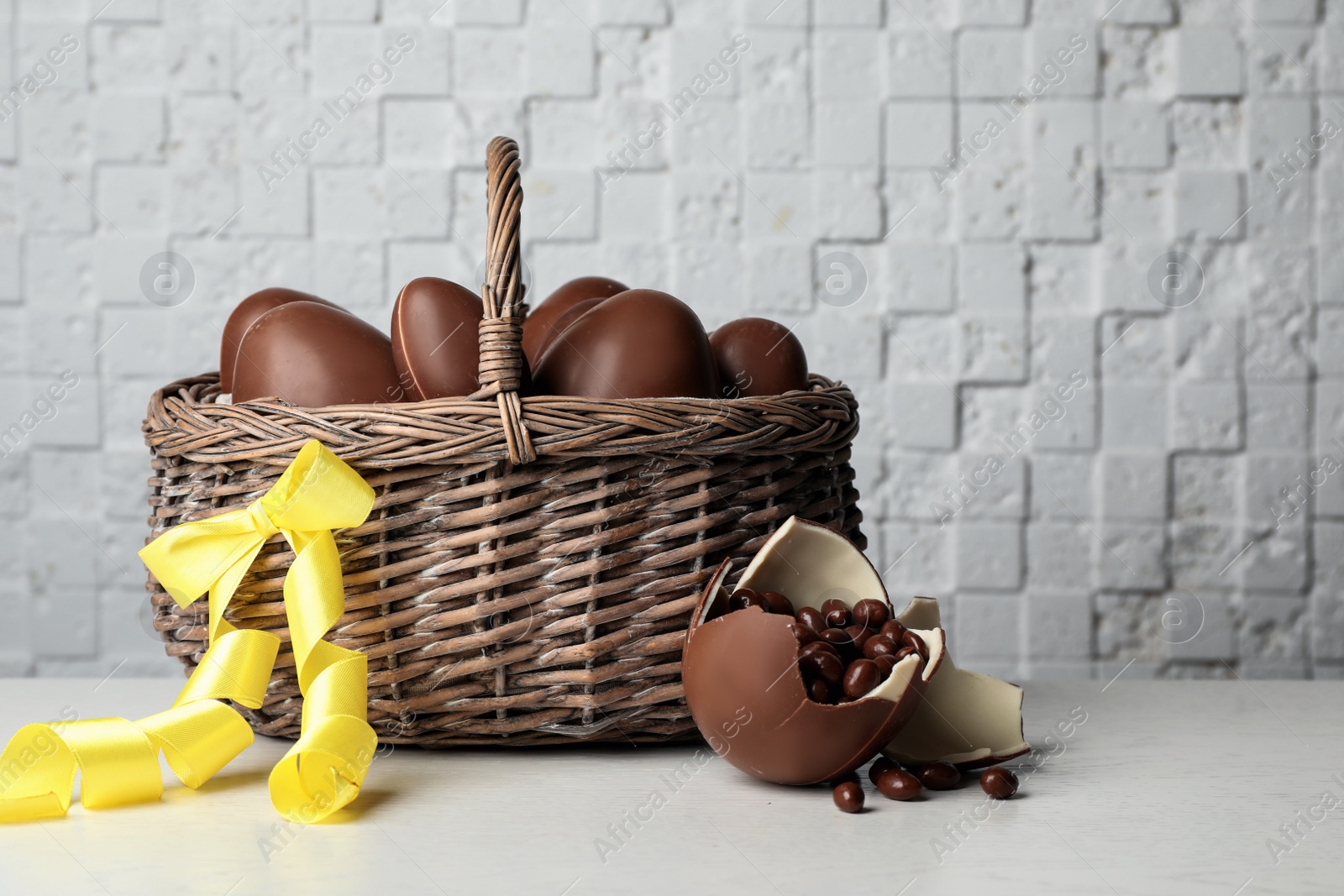 Photo of Wicker basket with sweet chocolate Easter eggs on table against light background