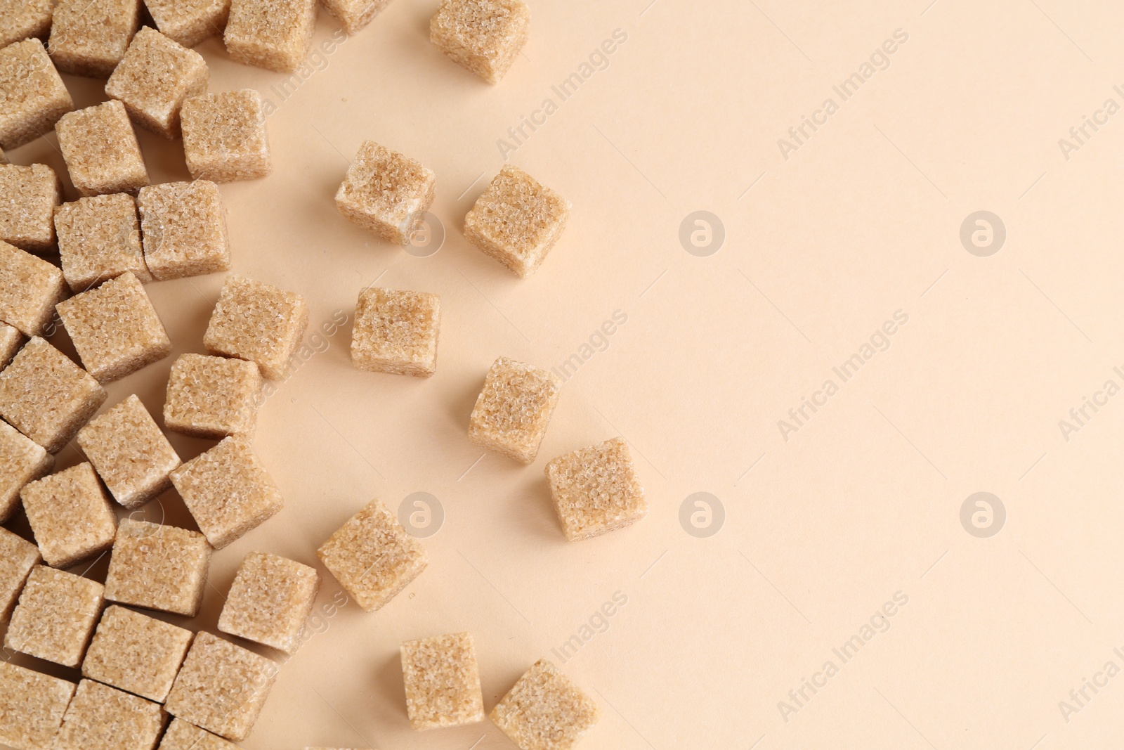 Photo of Brown sugar cubes on beige background, top view. Space for text