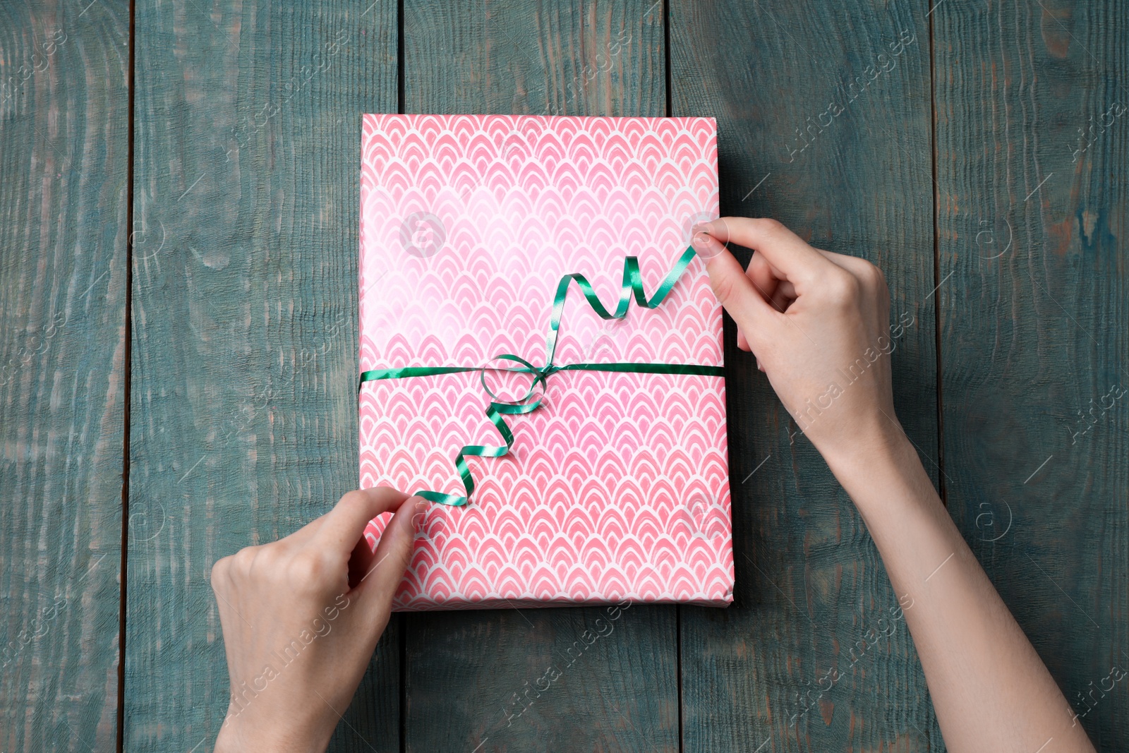 Photo of Woman wrapping gift with beautiful paper and ribbon at light blue wooden table, top view