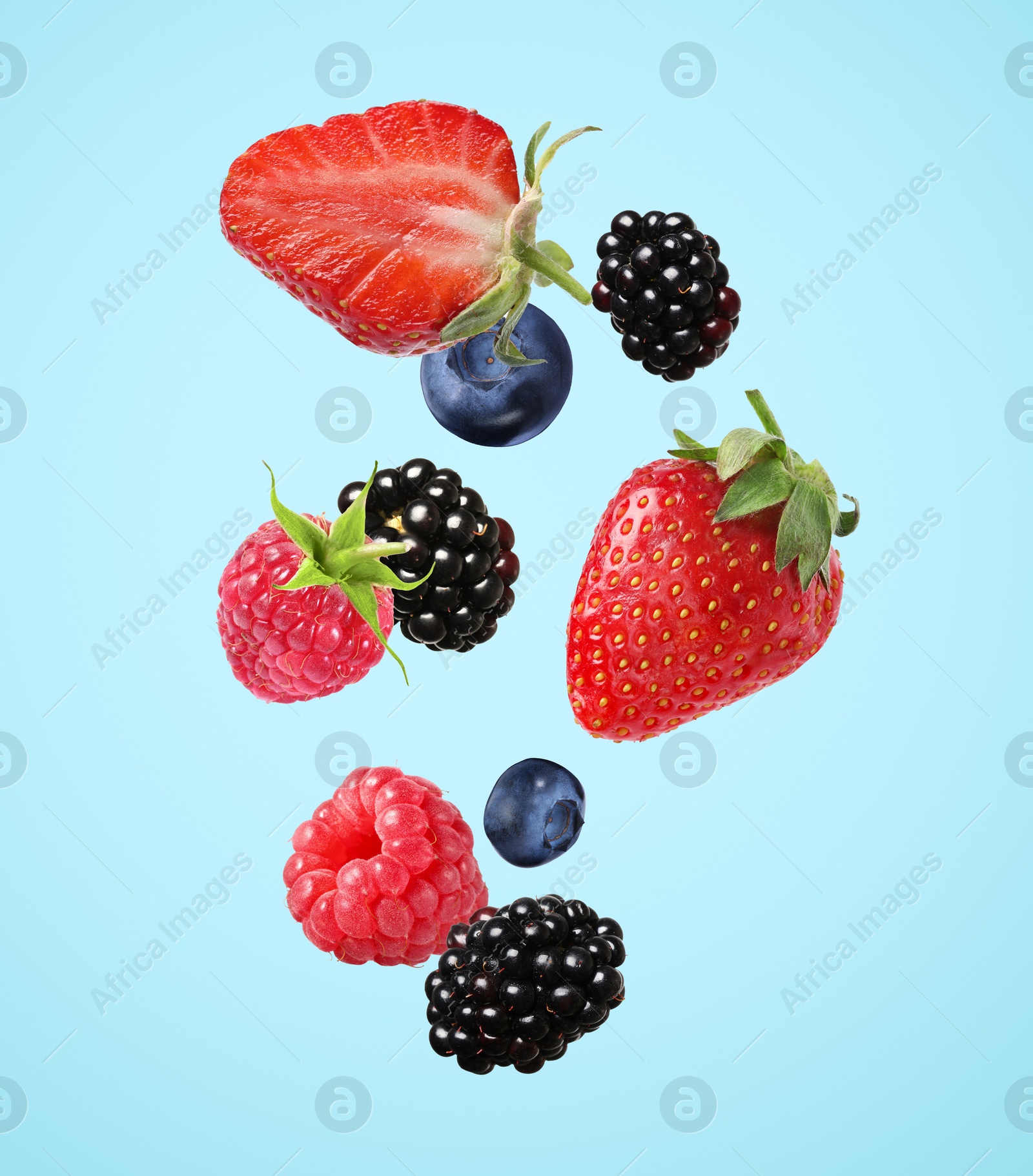 Image of Many different fresh berries falling on light blue background