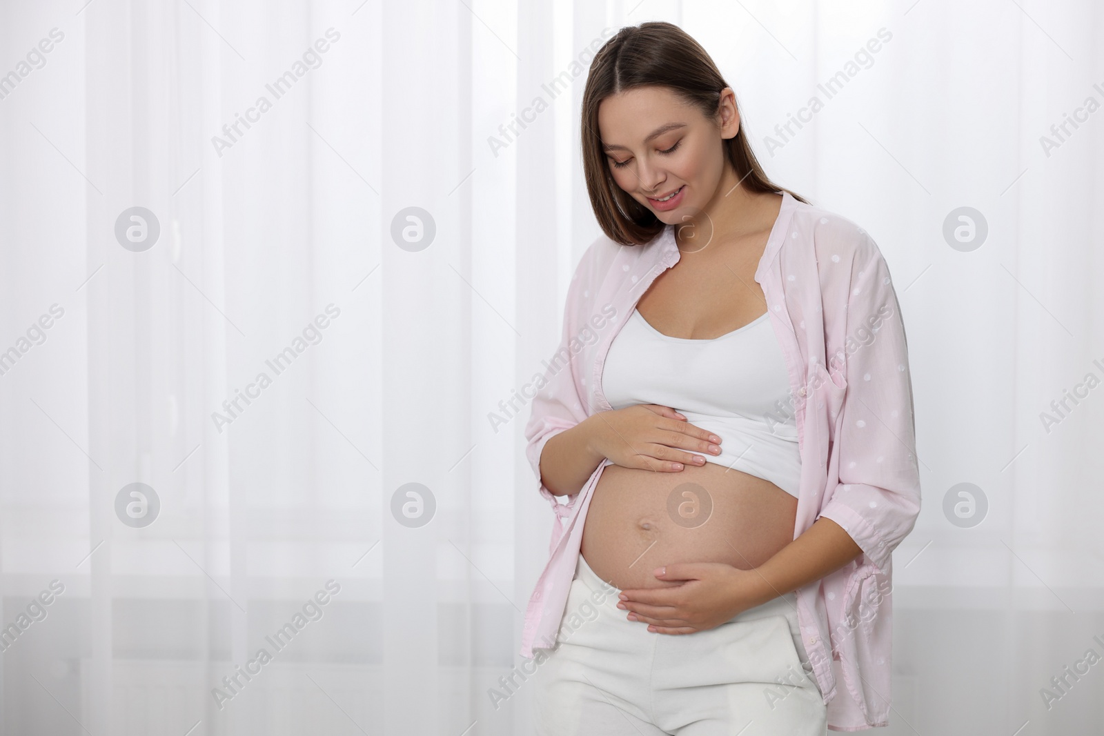 Photo of Beautiful pregnant woman near window indoors, space for text