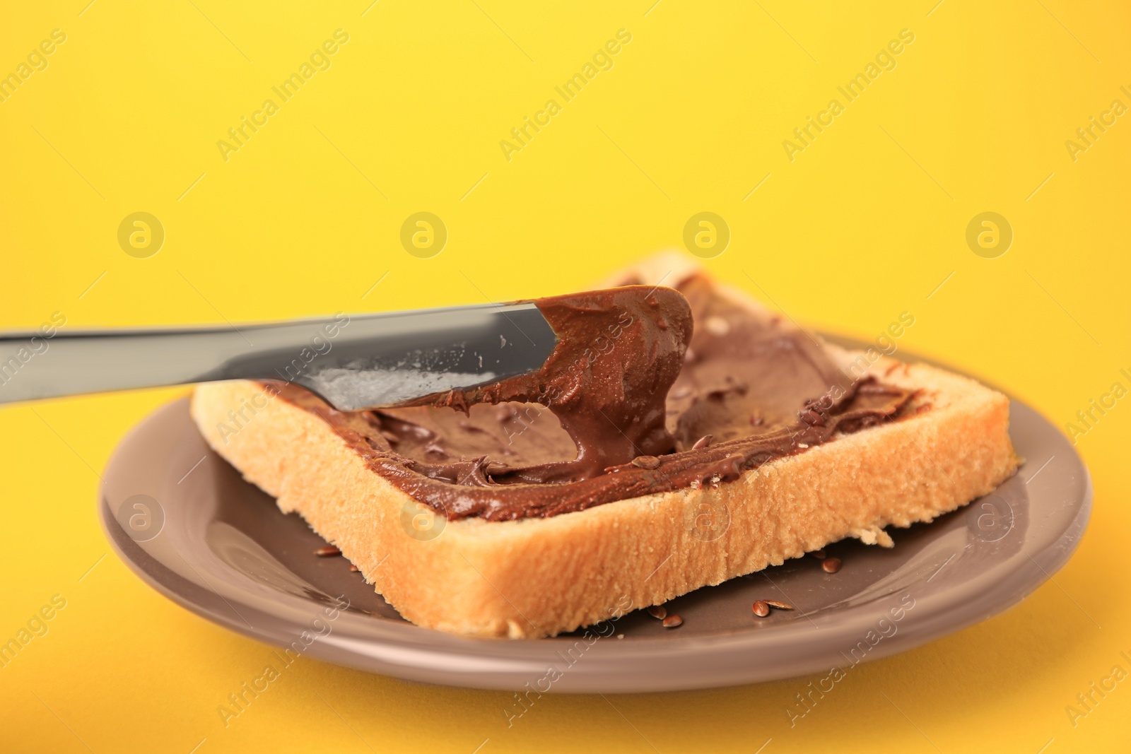 Photo of Spreading chocolate paste onto bread on yellow background, closeup