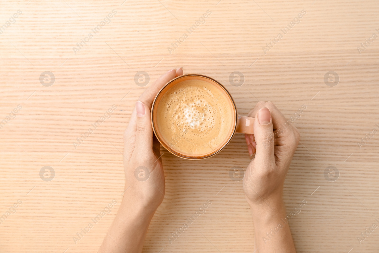 Photo of Woman with cup of aromatic hot coffee at wooden table, top view